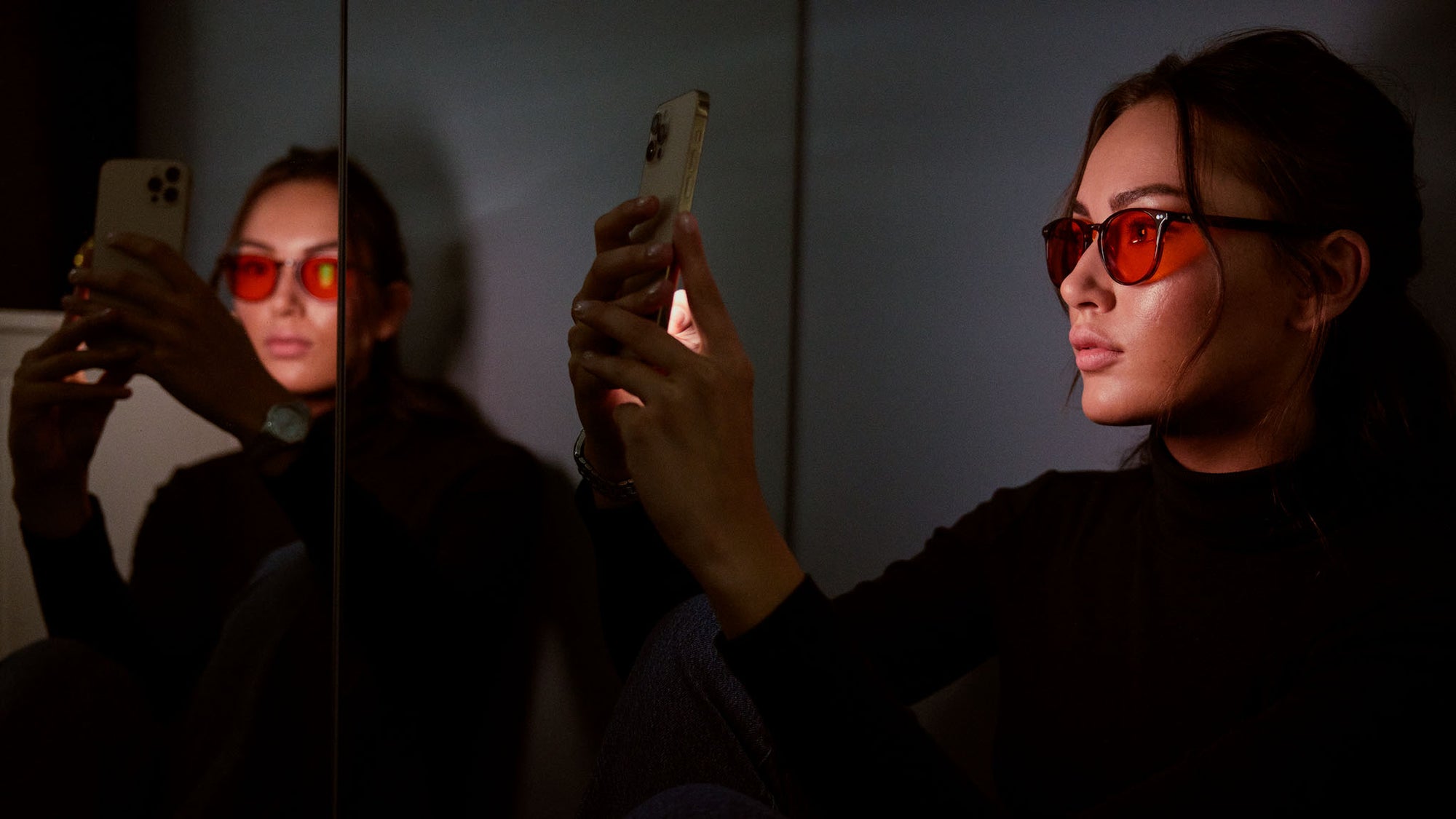 Woman wears Filter Optix blue blocking glasses while staring at her phone at night, to improve her circadian rhythm and get better sleep quality 