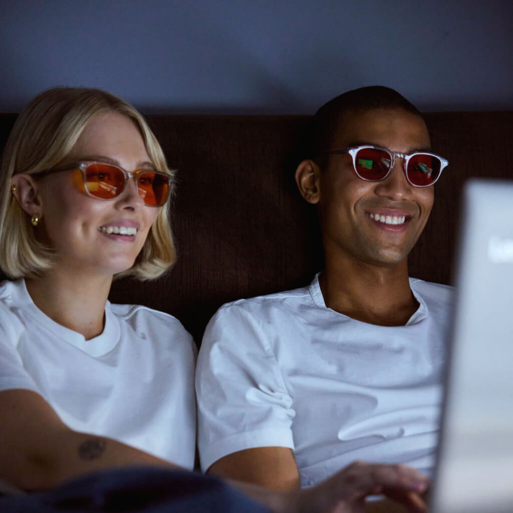 Couple wearing orange blue light blocking glasses while using a laptop at night